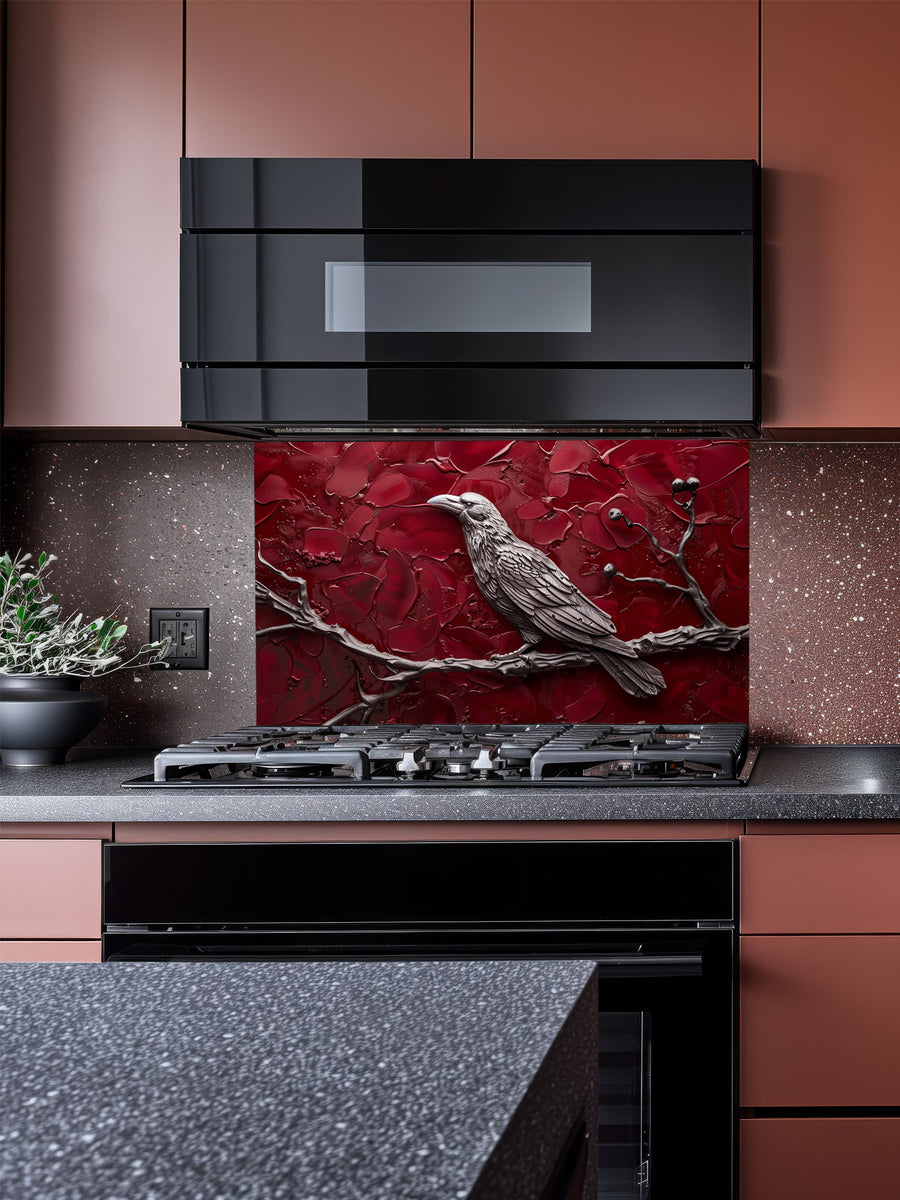 Tempered glass kitchen backsplash featuring a highly realistic 3D illusion of a sculpted metallic raven perched on a branch with berries against a heavily textured, thick impasto crimson red background, installed behind a modern black stove.