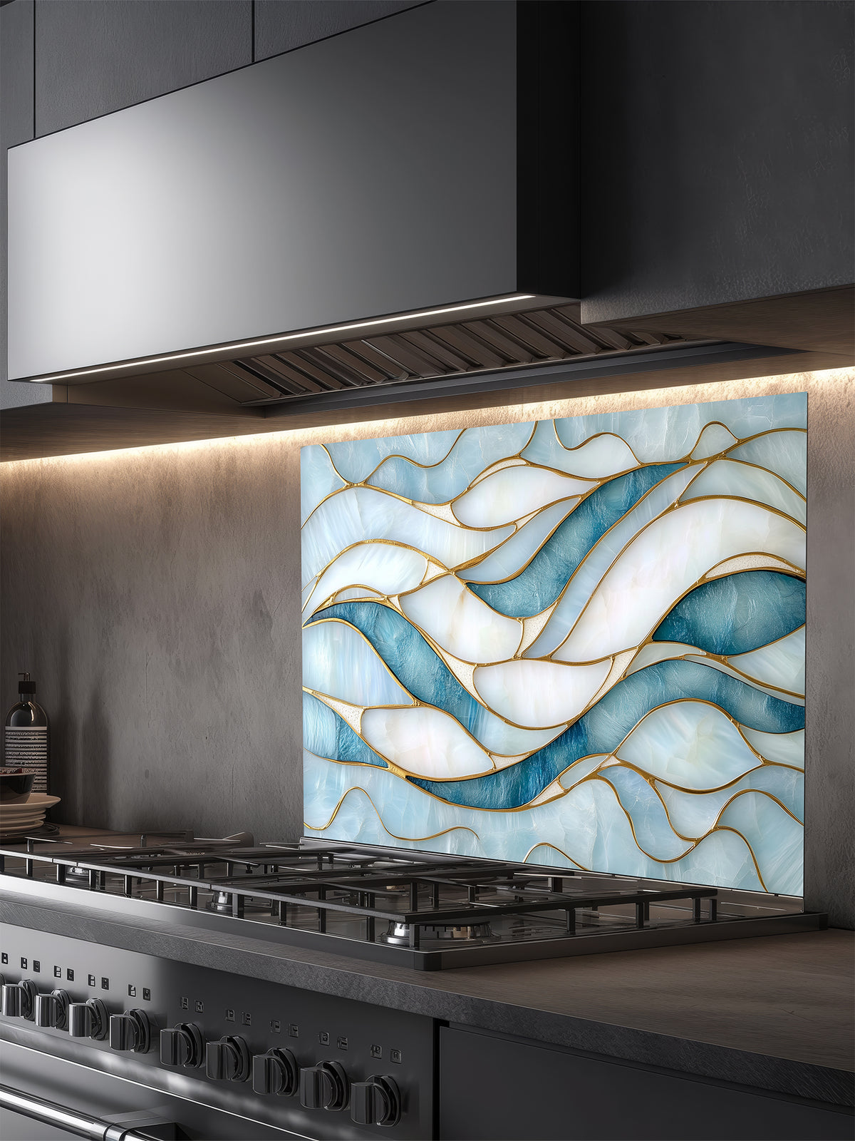 Tempered glass kitchen backsplash featuring a calming modern abstract wave design in faux stained glass with blue, teal, and pearlescent white sections separated by elegant gold lines, installed behind a modern stainless steel stove.