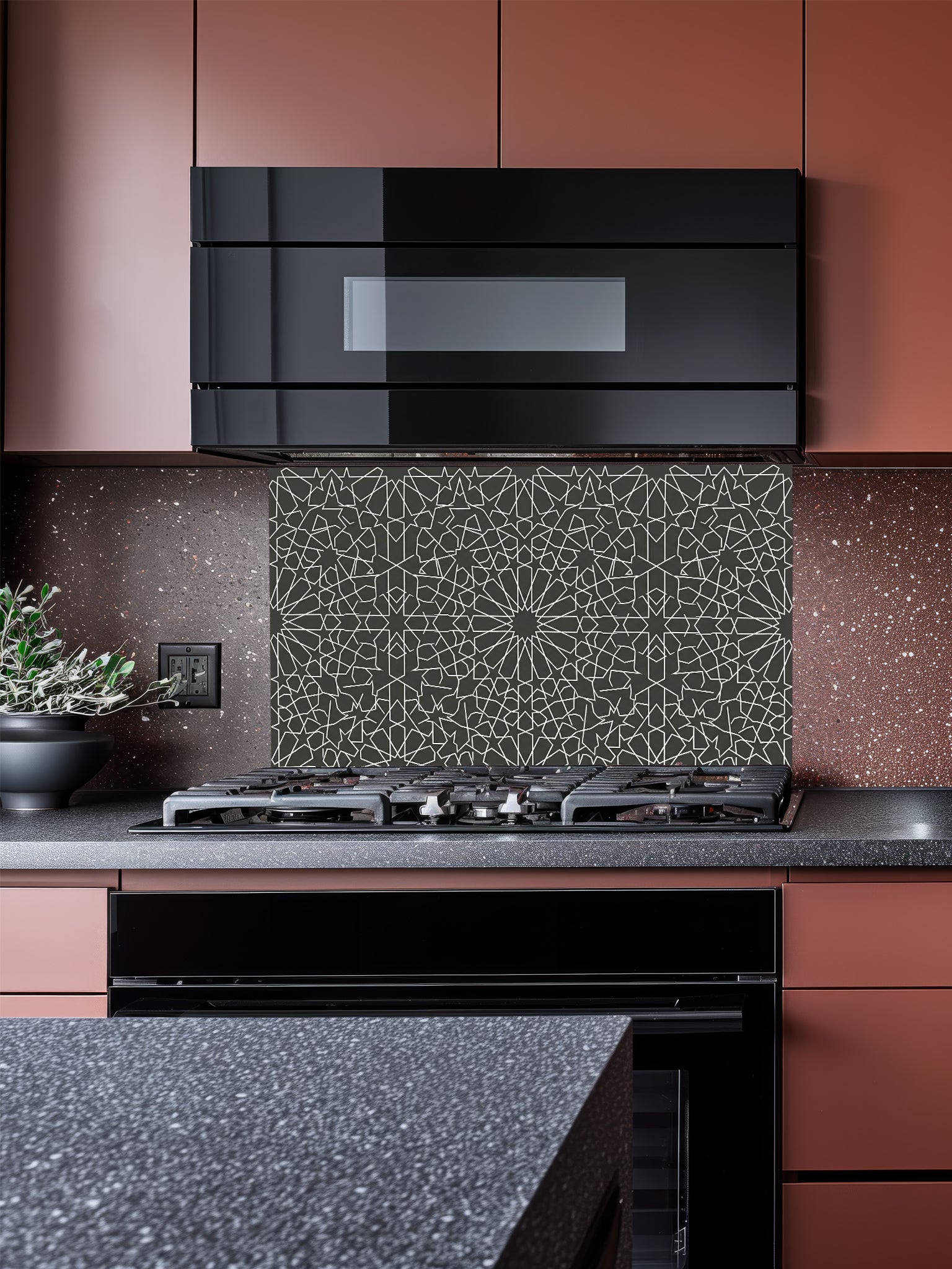 A modern minimalist kitchen featuring a sleek tempered glass backsplash with a charcoal grey and white Moroccan geometric star pattern, installed behind a black stove.