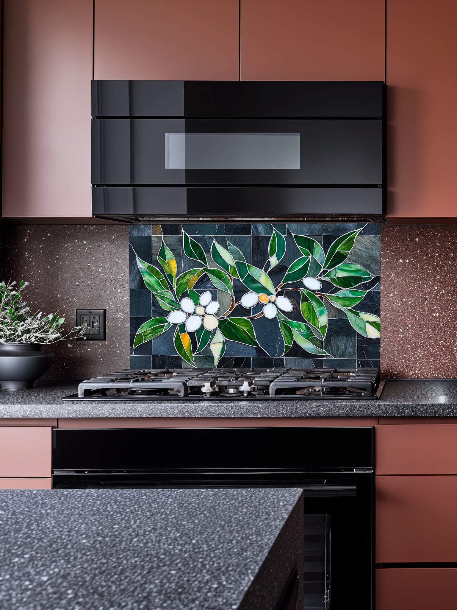 Tempered glass kitchen backsplash featuring a highly realistic 3D illusion of stained glass white blossoms and emerald green leaves integrated into a background of dark charcoal grey textured slate tiles, installed behind a modern black stove.