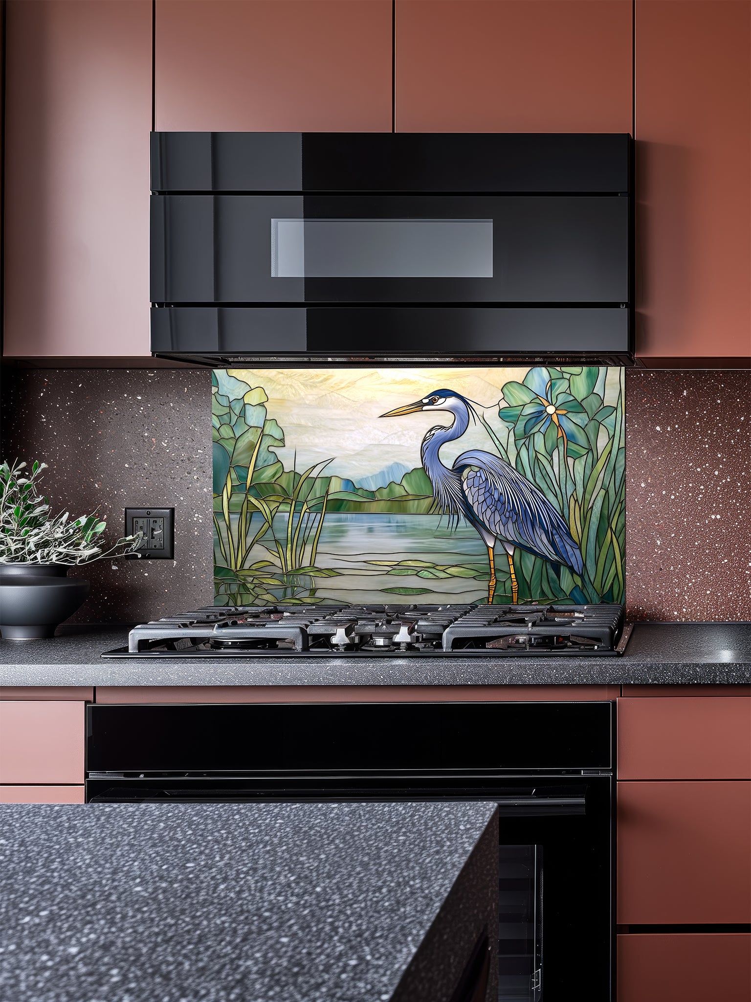 Tempered glass kitchen backsplash featuring a bright faux stained glass design of a majestic blue heron standing among lily pads against a glowing sunrise and mountain landscape, installed behind a modern stainless steel stove.