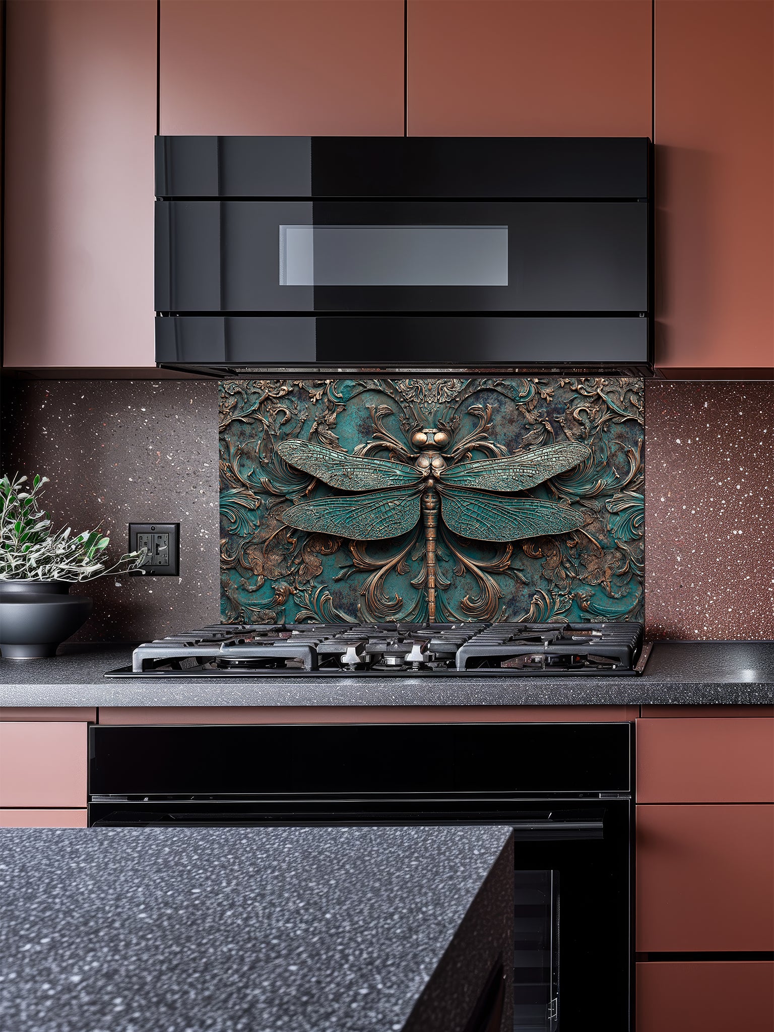 Tempered glass kitchen backsplash featuring a highly realistic 3D faux metal relief design of a detailed dragonfly and ornate antique bronze baroque scrollwork over a textured oxidized teal background, installed behind a modern stainless steel stove.
