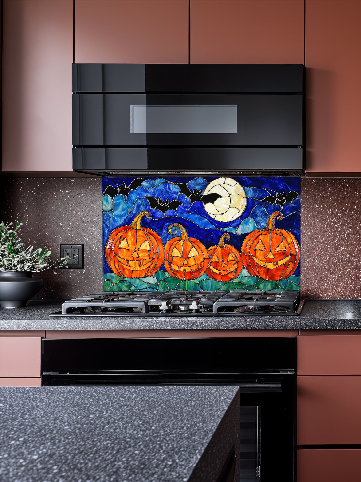 A festive kitchen featuring a tempered glass backsplash with a stained glass effect illustration showing four glowing jack-o'-lanterns, flying bats, and a full moon, installed behind a black stove.