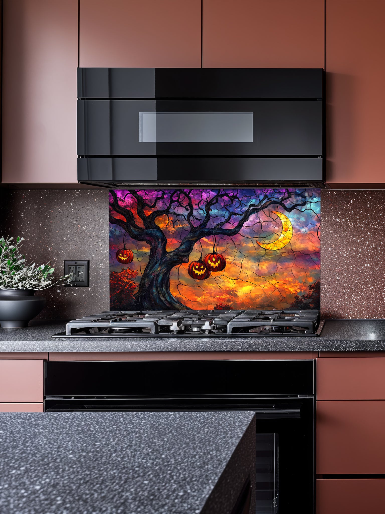 A festive kitchen featuring a tempered glass backsplash with a stained glass effect illustration showing a spooky twisted tree with hanging glowing pumpkins and a crescent moon against a purple and orange twilight sky, installed behind a black stove.
