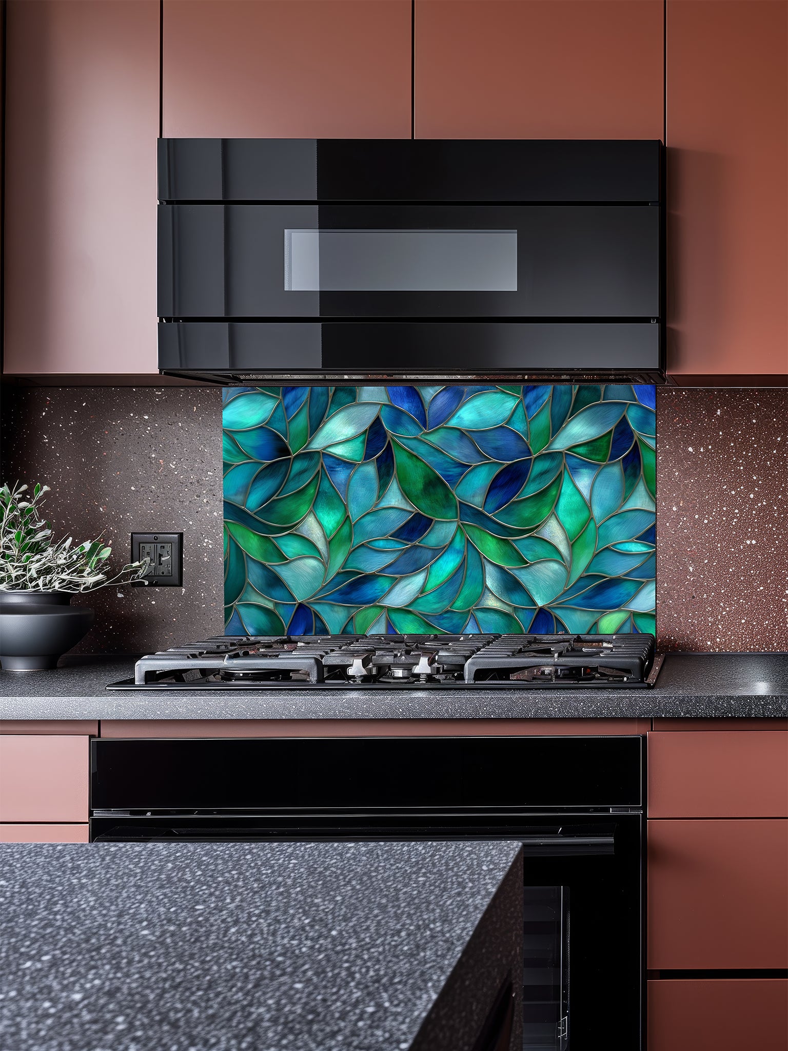 Tempered glass kitchen backsplash featuring a vibrant botanical stained glass effect with overlapping leaves in shades of teal, blue, and emerald green, installed behind a modern stainless steel stove.