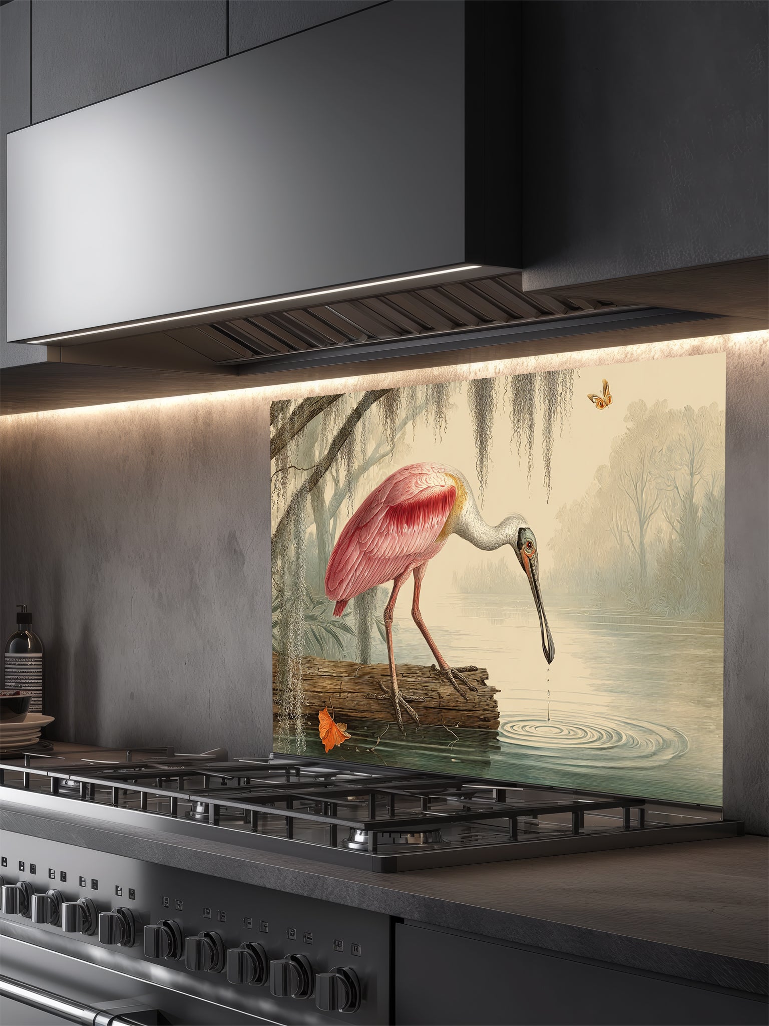 Tempered glass kitchen backsplash featuring a highly realistic illusion of a vintage Audubon-style naturalist illustration showing a beautiful pink roseate spoonbill bird wading in a swamp with weeping Spanish moss against an aged parchment background, installed behind a modern black stove.