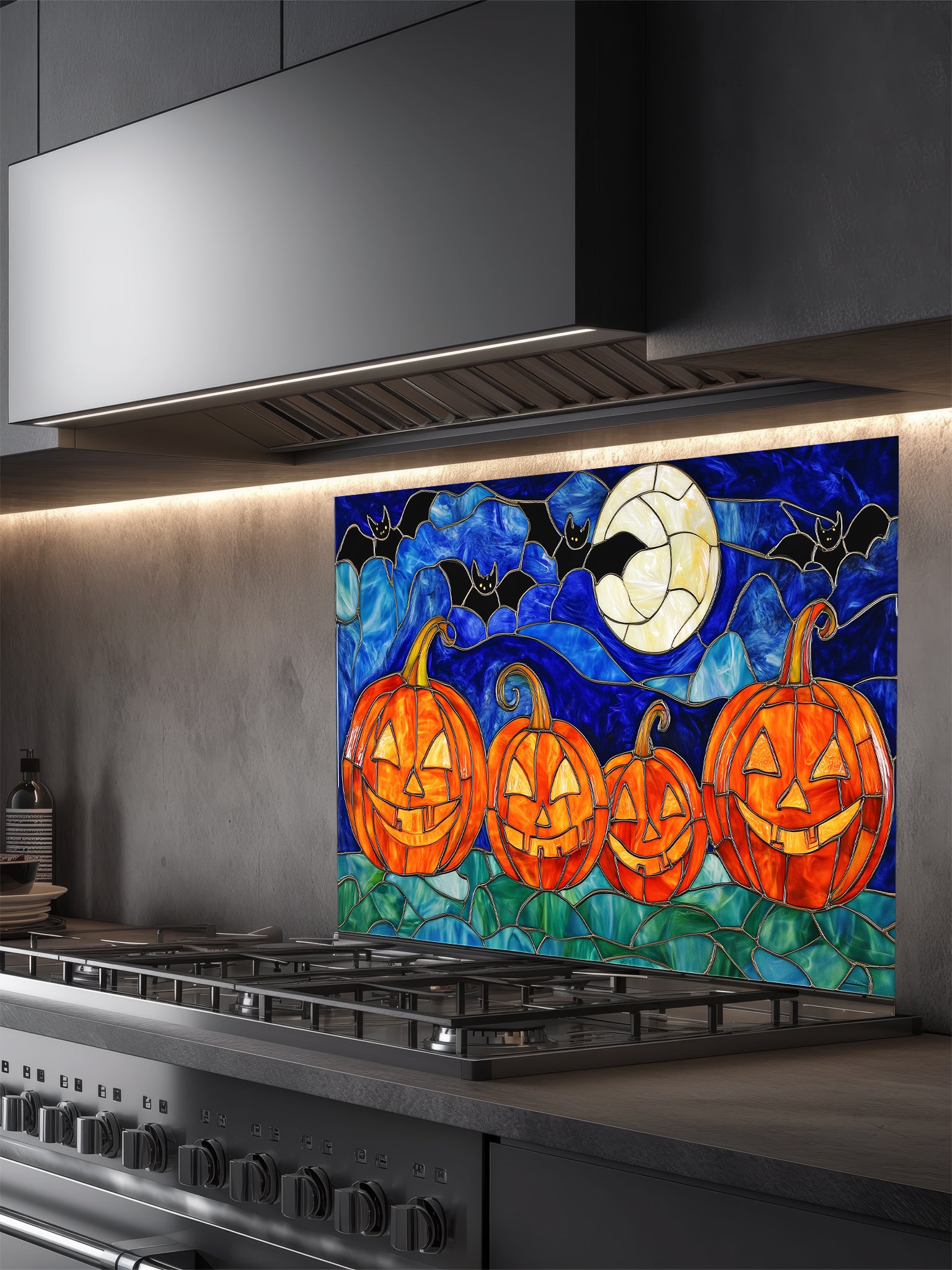Halloween-themed glass splashback with pumpkins and moon above a kitchen stove.