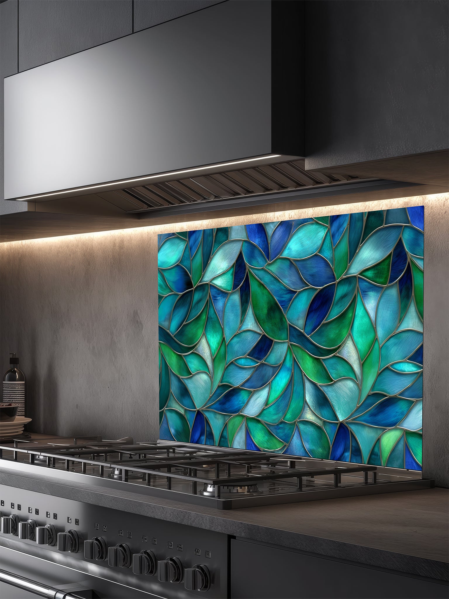 Tempered glass kitchen backsplash featuring a vibrant botanical stained glass effect with overlapping leaves in shades of teal, blue, and emerald green, installed behind a modern stainless steel stove.
