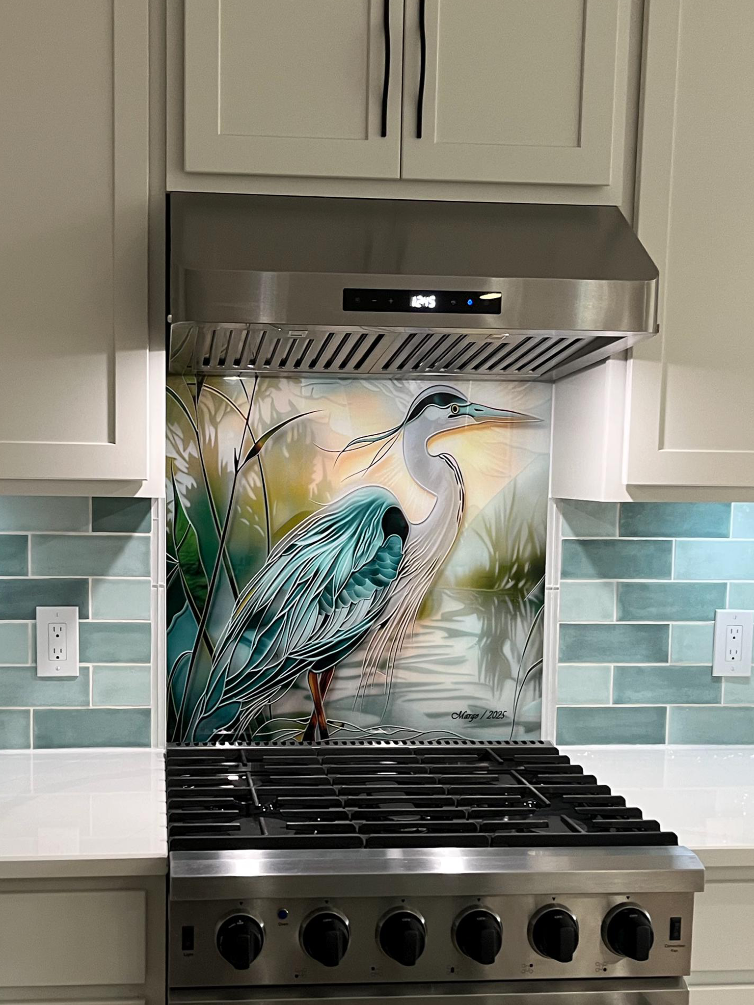 Tempered glass kitchen backsplash featuring a bright faux stained glass design of a majestic blue heron standing in a wetland, with bright sun rays radiating like a halo from behind its head, installed behind a modern stainless steel stove.