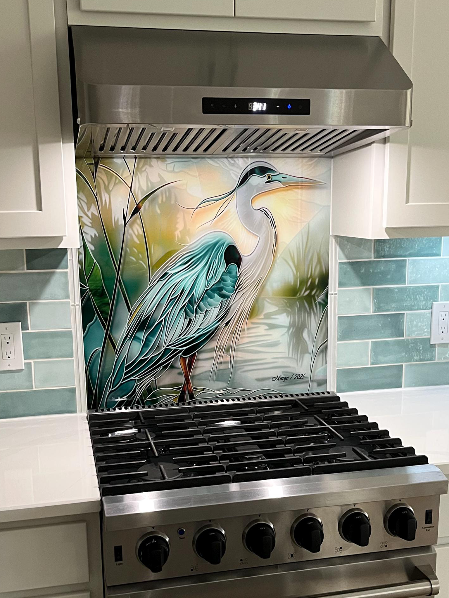 Tempered glass kitchen backsplash featuring a bright faux stained glass design of a majestic blue heron standing in a wetland, with bright sun rays radiating like a halo from behind its head, installed behind a modern stainless steel stove.