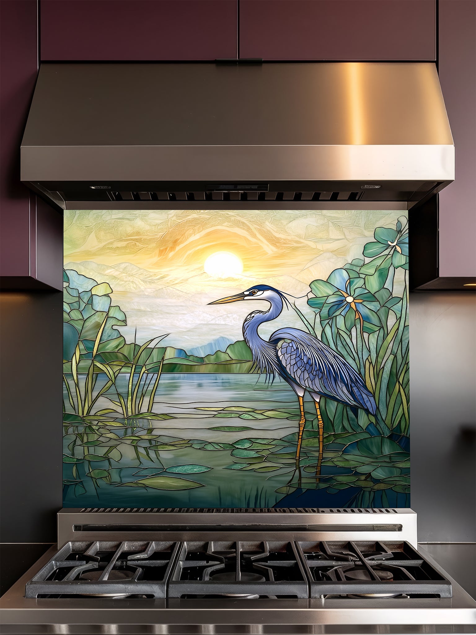 Tempered glass kitchen backsplash featuring a bright faux stained glass design of a majestic blue heron standing among lily pads against a glowing sunrise and mountain landscape, installed behind a modern stainless steel stove.