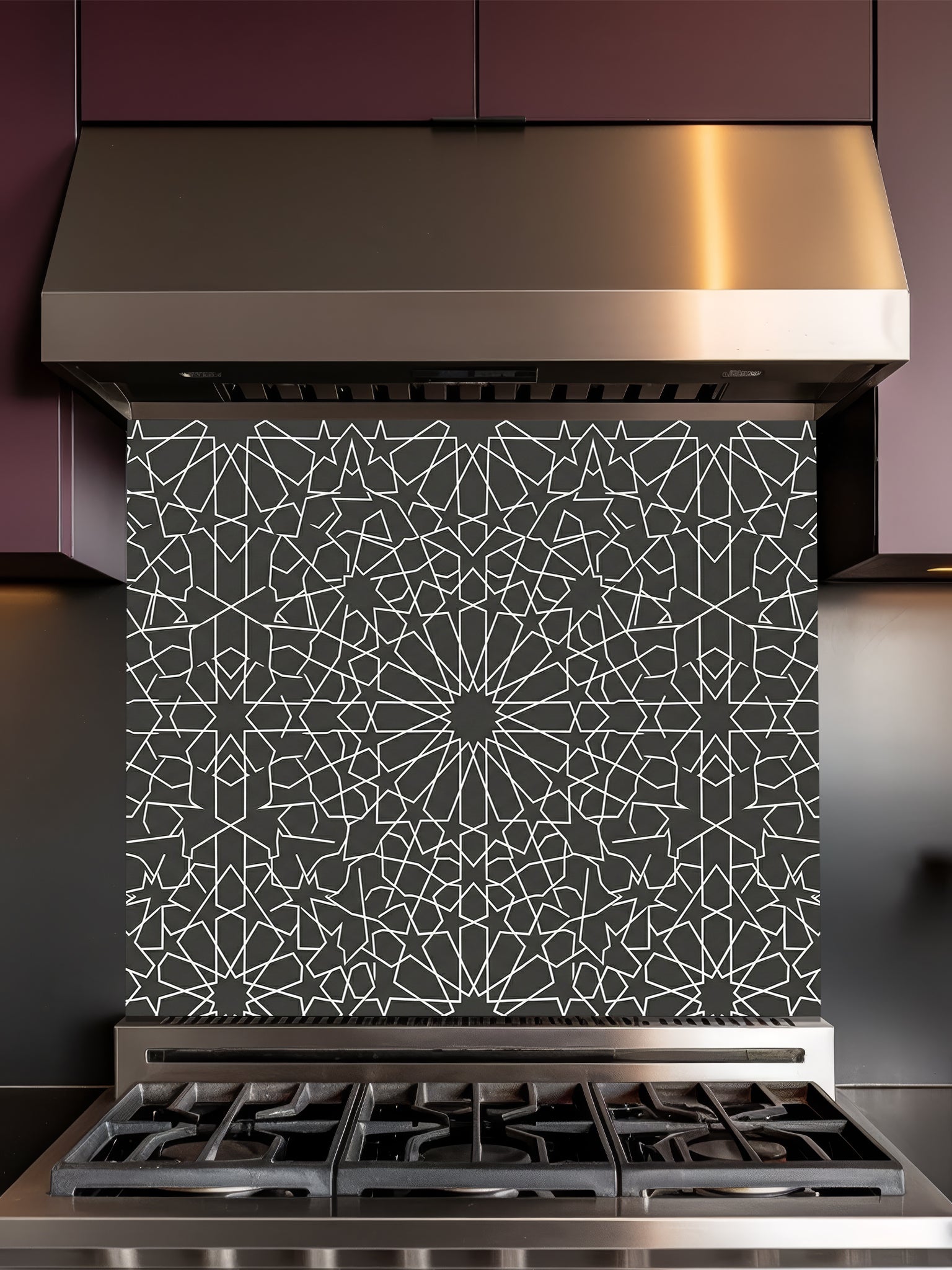 Stainless steel range hood with geometric patterned backsplash above a stove.