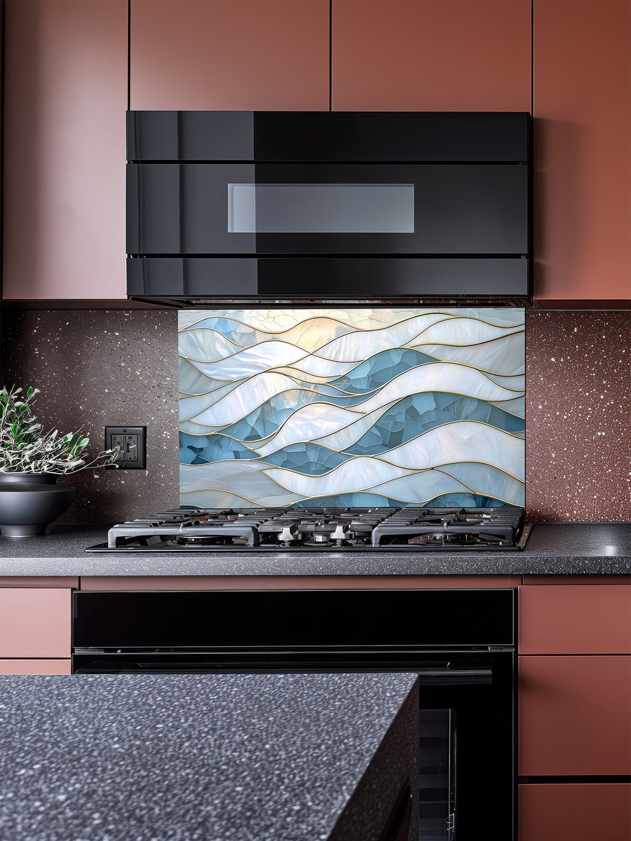 Tempered glass kitchen backsplash featuring a serene faux stained glass design of layered, flowing waves in icy blue and pearlescent white, separated by elegant gold outlines, installed behind a modern stainless steel stove.
