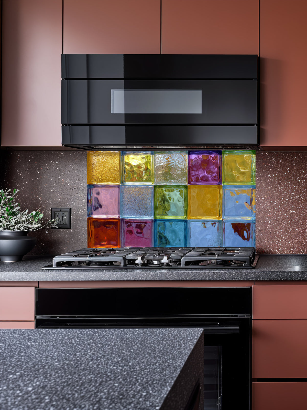 Tempered glass kitchen backsplash featuring a highly realistic 3D illusion of colorful architectural glass blocks in vibrant translucent hues of blue, green, yellow, and purple with wavy textures, installed behind a modern stainless steel stove.
