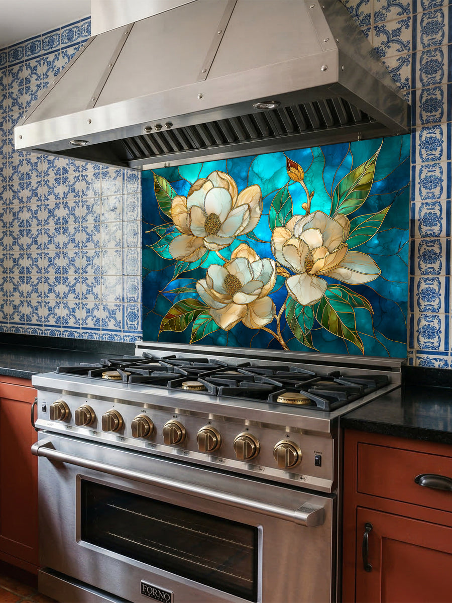 Tempered glass kitchen backsplash featuring a highly realistic 3D illusion of stained glass art showing elegant white magnolia blossoms with gold outlines against a swirling deep blue and teal background, installed behind a modern stainless steel stove.