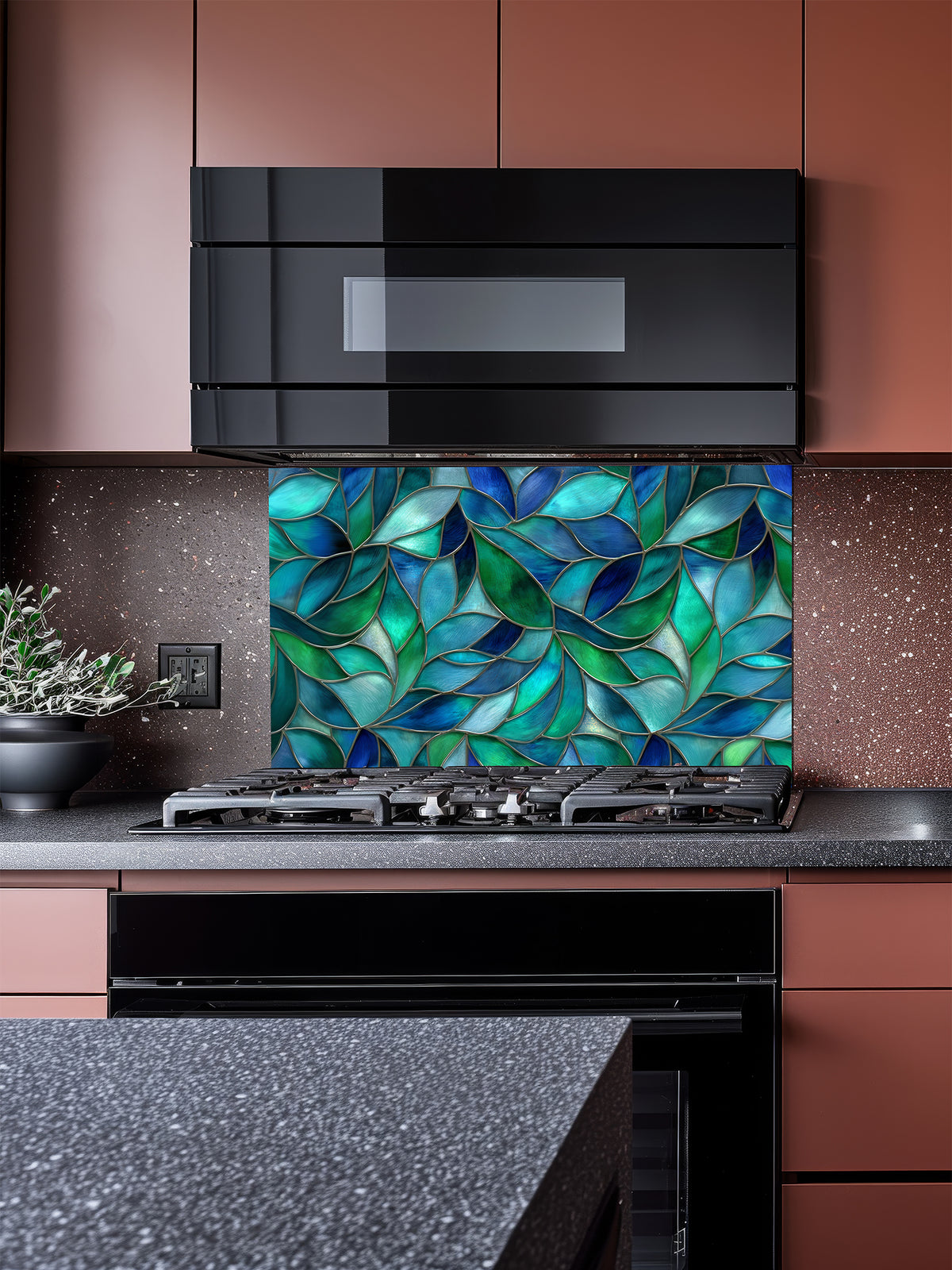 Tempered glass kitchen backsplash featuring a vibrant botanical stained glass effect with overlapping leaves in shades of teal, blue, and emerald green, installed behind a modern stainless steel stove.